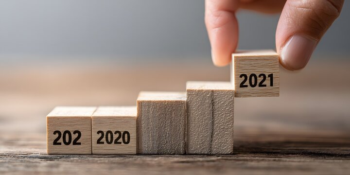 Hand placing wooden cube with 2021 atop ascending stair of blocks labeled 2020 and 202.