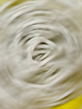 An abstract photograph featuring a strong radial spin blur centered on light grey and soft yellow tones.