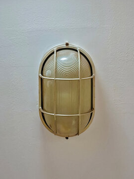 An oval vintage-style wall light fixture with a protective metal cage mounted against a textured white background.