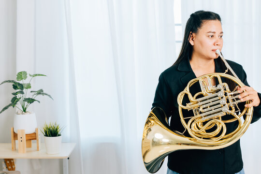 Dressed in black, a woman blows a gleaming French horn in gold