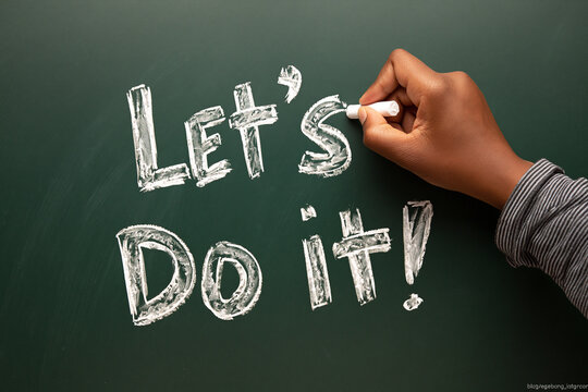 Hand writes 'Let's Do It!' with chalk on a dark green chalkboard. Motivational phrase for action and teamwork.