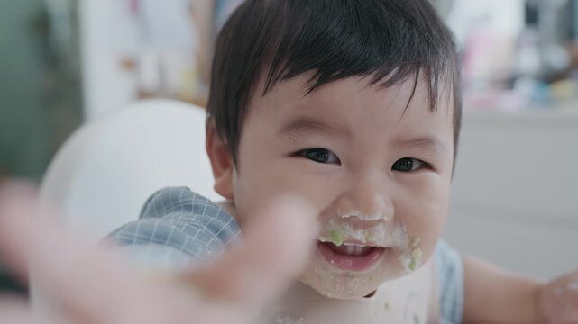 Asian baby boy self feeding sweet corn using baby led weaning method at home.	