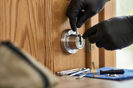 Locksmith using professional tools to pick a door lock, closeup of hands in black gloves working on a wooden door mechanism