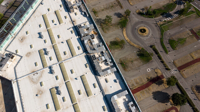 Aerial view of a retail shopping center roof featuring HVAC units, ventilation systems, and skylights adjacent to a circular road intersection in Assago, Lombardy, Italy.