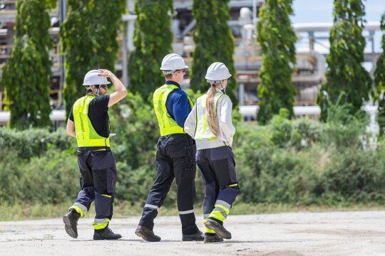 Oil refinery engineers team walking together at industrial plant, Petroleum plant workers in safety gear walking outdoors at facility, Energy industry professionals inspecting industrial site walking