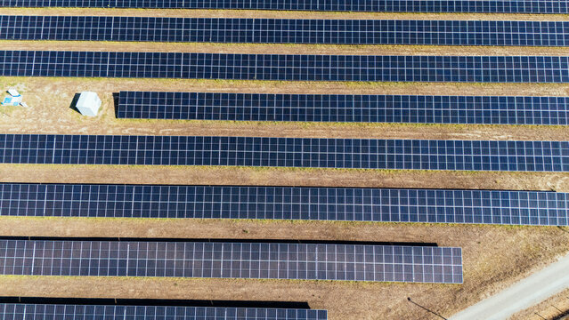 Aerial view of rows of photovoltaic solar panels installed in a field with dry grass and a small utility building in Indjija, Vojvodina, Serbia.