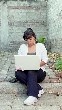 Woman sitting in her home patio using a laptop near a concrete block wall