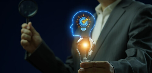 Close-up vertical shot of hand holding magnifying glass to inspect glowing lightbulb in human head profile thinking idea. Cognitive thought process analysis, intellect innovation, and wisdom concept. © kobps2