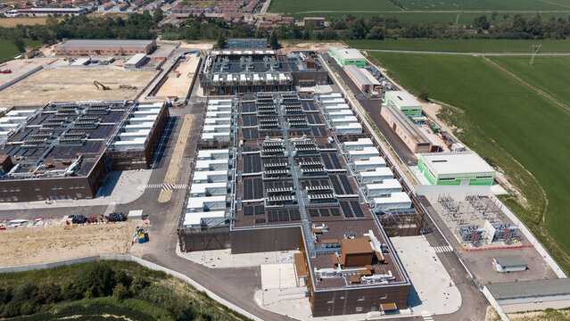 Aerial view of the Stack Infrastructure MIL04 Campus data center, featuring industrial buildings with rooftop cooling units, surrounded by fields in Vellezzo Bellini, Lombardy, Italy.