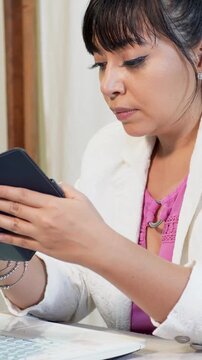 A young woman checks her cell phone while working on a laptop from home.