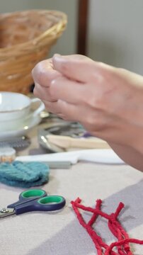 Female hands making handmade earrings with wooden pieces and red thread