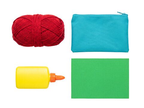 A vibrant flat lay of craft supplies featuring red yarn, a turquoise pencil case, yellow glue, and green foam paper.