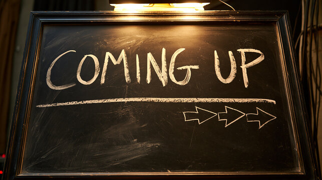 Coming up written in chalk on a dark blackboard with arrows. Use this image for marketing announcements or event promotion campaigns.
