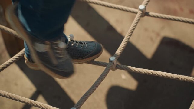 Close up of young boy carefully stepping across thick rope obstacles in outdoor playground. focus remains on his feet and textured ropes highlighting movement through challenging equipment