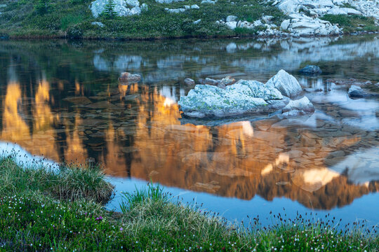 A clear alpine pond reflects golden mountain slopes and rocks in the Monashee wilderness.
