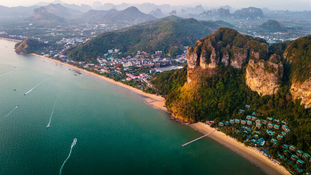 Aerial view of the dramatic limestone cliffs, sandy beach, and resort buildings along the coastline in Krabi, Thailand.
