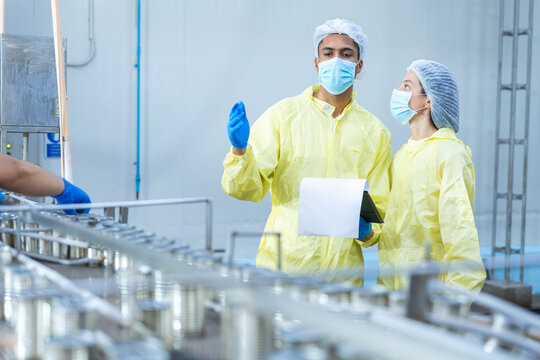 Food canning factory quality control inspectors checking production line, factory workers with clipboard inspecting canned food, industrial manufacturing plant inspectors discussing production process