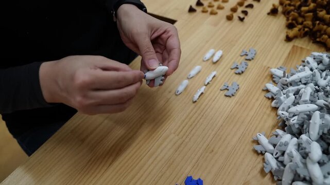 Worker sorting small airplane and oval shaped novelty erasers by hand at a Japanese factory table