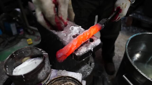 Blacksmith sprinkling borax flux over a long glowing blade blank on an anvil beside a quenching bucket