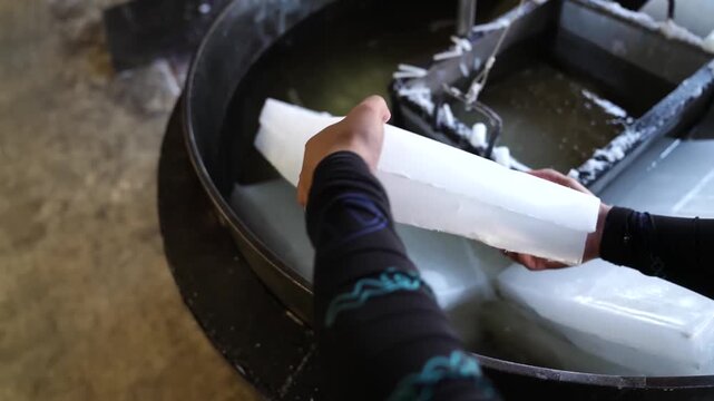 Worker lifting a large solidified white wax block from a cooling water tank at a Japanese candle factory