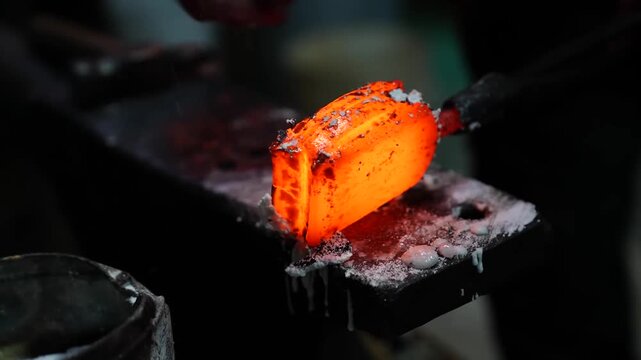 Extreme close up of a glowing layered steel billet showing pattern welded lines on a forging die