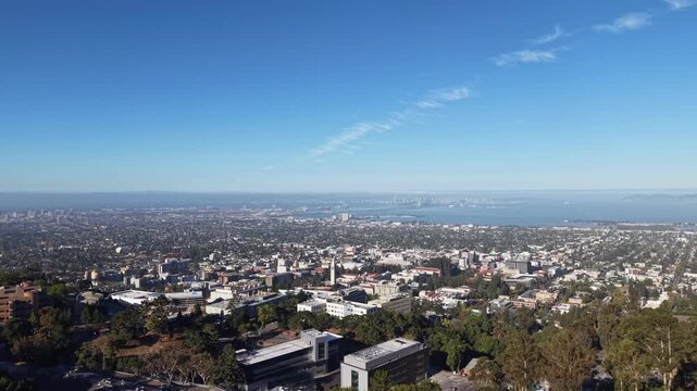 Wide aerial shot revealing the University of California Berkeley campus, the city of Berkeley, and the distant San Francisco Bay skyline on a beautiful clear day with blue skies