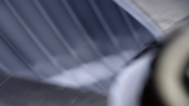 Gray oscillating fan blades turn behind a grille in soft focus indoors.