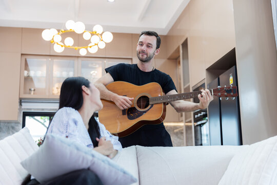 Young multicultural couple enjoying live acoustic guitar music together in a bright modern home. Romantic relationship