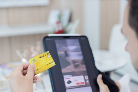 Young man holding a credit card while using a laptop to make an online purchase from home. E-commerce checkout, secure digital payment, internet banking, cashless transaction and consumer technology .