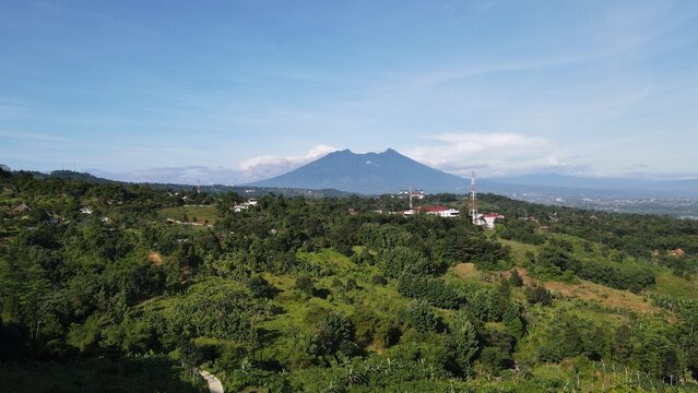Aerial view of the lush green Sentul highlands with Mount Pancar in the background, featuring dense tropical vegetation and rolling hills in Babakan Madang, West Java, Indonesia.