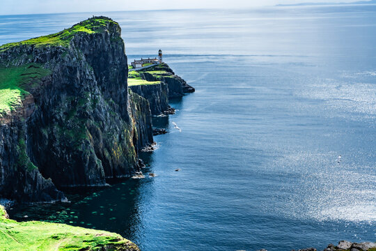 Neist Point Lighthouse on steep cliffs with sparkling blue sea on Isle of Skye