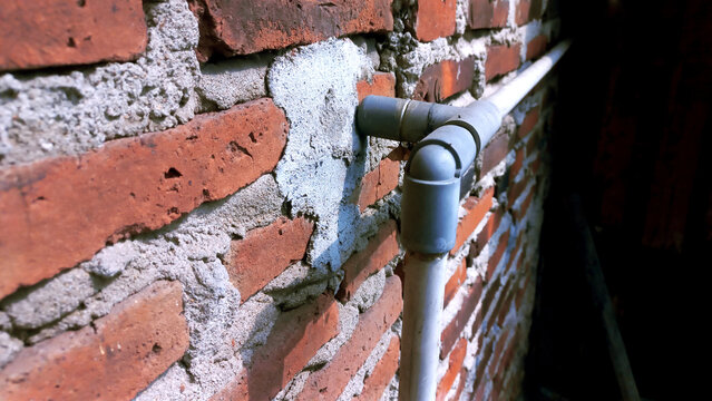 Gray PVC water pipe connection installed on a red brick wall.