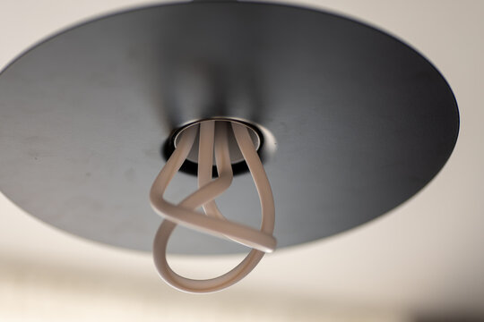Close up of a modern ceiling lamp with circular metal shade and curved LED tubes, minimalist interior lighting design.