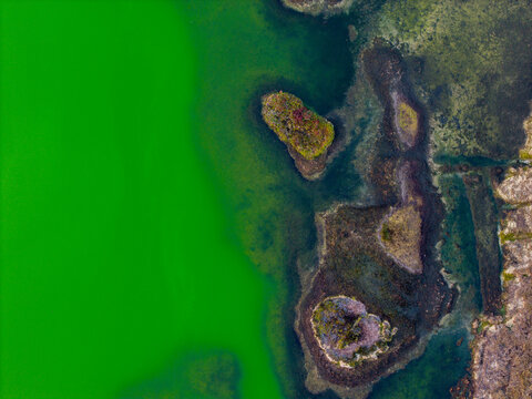Aerial view of Telaga Warna Dieng featuring its vibrant green volcanic lake water, small vegetated islands, and rocky shoreline in Indonesia.