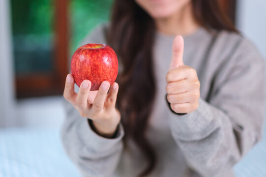 Closeup image of a woman showing thumbs up hand sign while holding a red apple