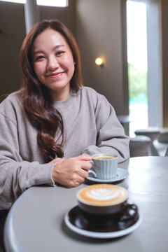 Portrait image of a woman holding and drinking coffee with friend in cafe