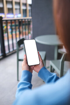 Vertical mockup image of a woman holding and using mobile phone with blank desktop screen in cafe
