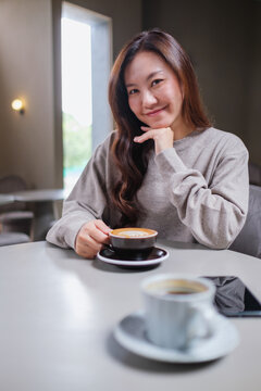 Portrait image of a woman holding and drinking coffee with friend in cafe