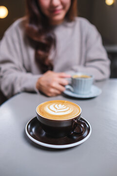 Vertical closeup image of a woman holding and drinking hot coffee in cafe