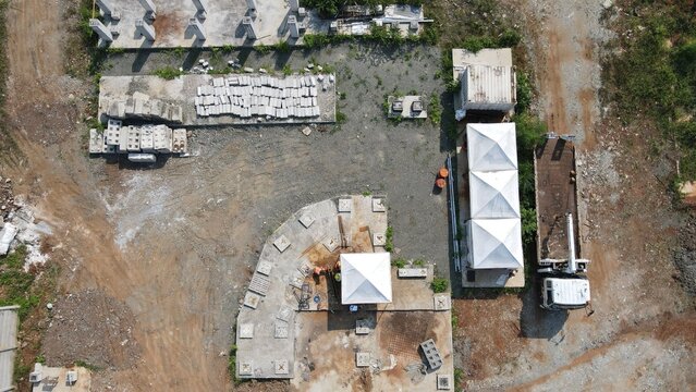 Aerial view of the Bambu Apus construction site featuring concrete blocks, white tents, and a parked truck in Kecamatan Cipayung, Daerah Khusus Ibukota, Indonesia.