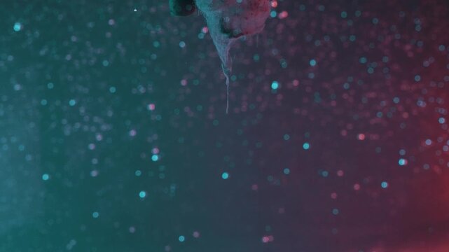 Abstract flowing paint forms dissolving in liquid with bright particles against a dark background in stunning slow motion.
