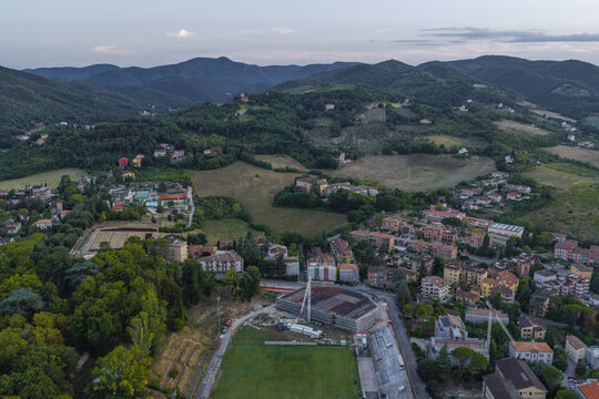 Aerial view of the town nestled in the rolling green hills of Umbria, featuring residential buildings, a construction site with a crane, and lush surrounding forests. Spoleto, Umbria, Italy.