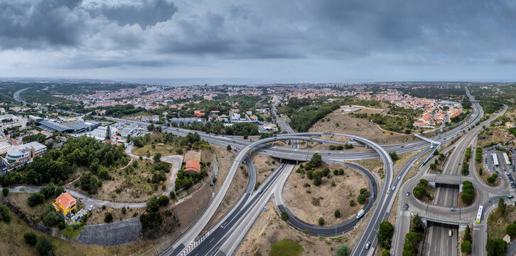 Aerial view of the A5 highway interchange with sweeping curves and surrounding urban landscape in Cascais, Lisboa, Portugal.