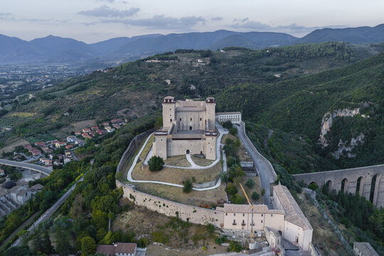 Aerial view of the historic Rocca Albornoziana fortress with its stone towers and defensive walls overlooking the surrounding hills and the Ponte delle Torri in Spoleto, Umbria, Italy.