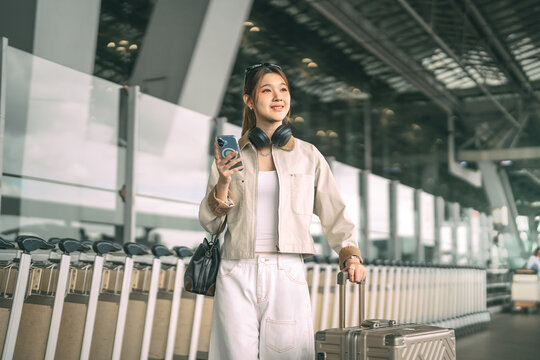 Young adult asian woman with travel luggage using smartphone app call taxi service transfer at international airport shuttle bus terminal
