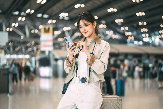 Young adult asian woman with travel luggage using smartphone app call taxi service transfer at international airport shuttle bus terminal