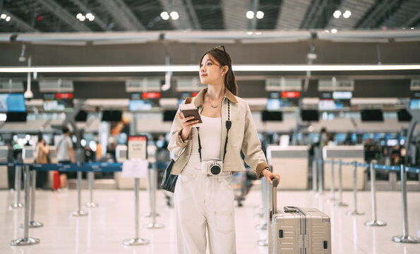 Young asian woman traveller to transit holding passport with boarding pass at ticket counter international airport terminal for departure