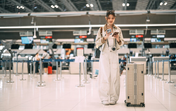 Young asian woman traveller to transit holding passport with boarding pass at ticket counter international airport terminal for departure