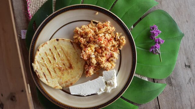 Traditional breakfast plate with arepa scrambled eggs and fresh white cheese served on monstera leaf.