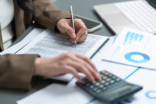 Businesswoman reviews financial records with a calculator and pen beside charts and reports, representing accounting, audit, bookkeeping, budget analysis, financial reporting and accuracy.